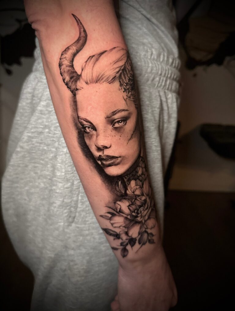 Portrait tattoo with horns and floral detail on a forearm