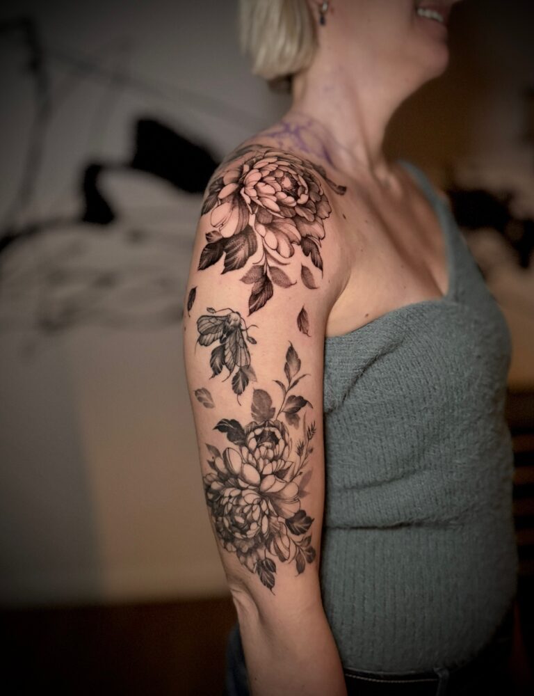 Large flowers and foliage tattooed over a shoulder and upper arm